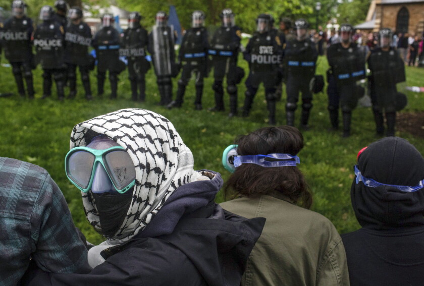 A pro-Palestinian demonstrator wears goggles and a mask as police with riot shields and protesters stand across from one another on the grounds of the University of Virginia, in Charlottesville, Va., where tents are set up, Saturday, May 4, 2024.