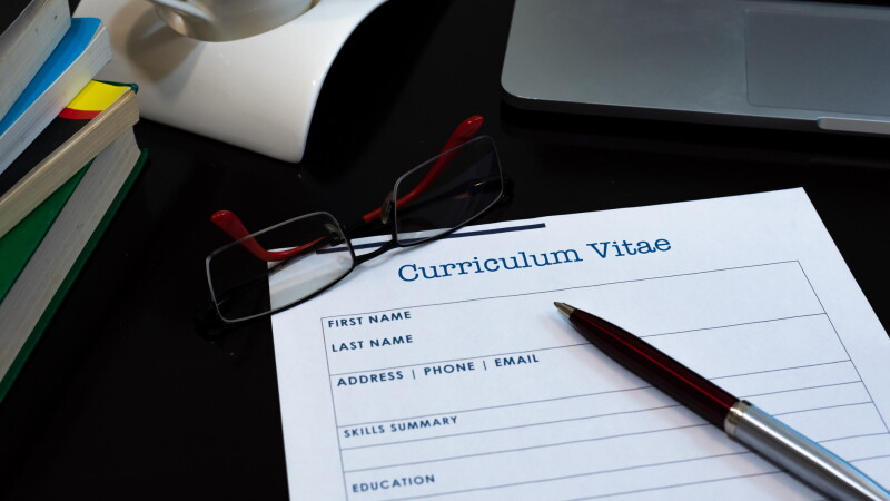 photograph of a curriculum vitae being filled out with pen, glasses, coffee