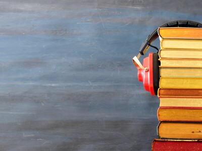 Relaxing with audiobooks concept with heap of books and vintage headphones. Dark background with large copy space.