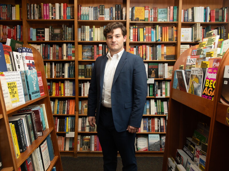 Theo Baker stands in a bookstore, amid shelves of books.